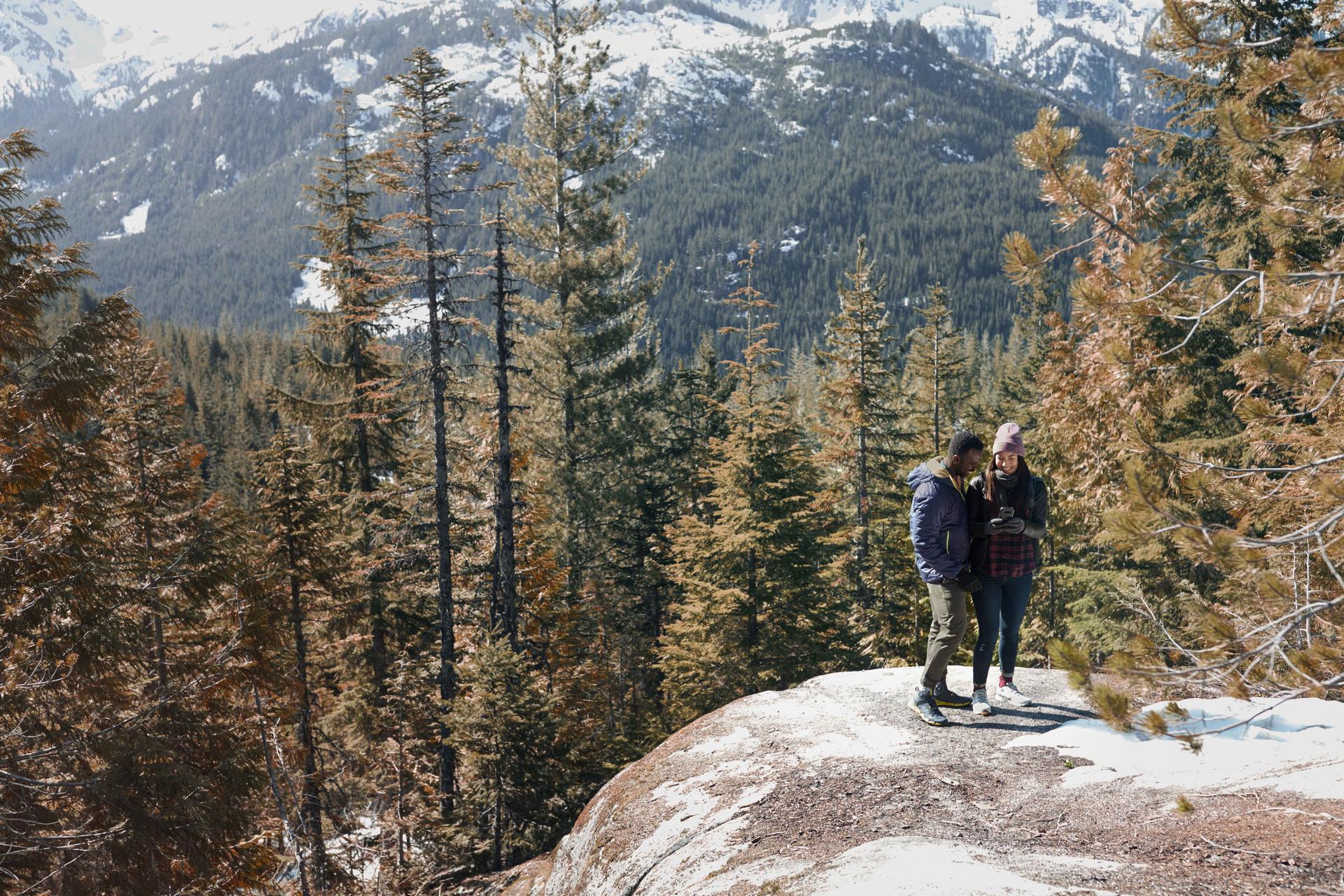 two people standing on a rock in the middle of the forest