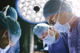 Close-up of surgeons in scrubs looking downward, illuminated by overhead surgical lights.